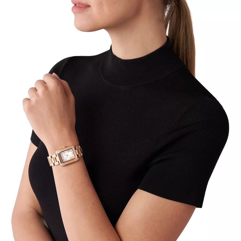 Michael Kors Emery rose gold-tone watch worn on woman's wrist with black sweater