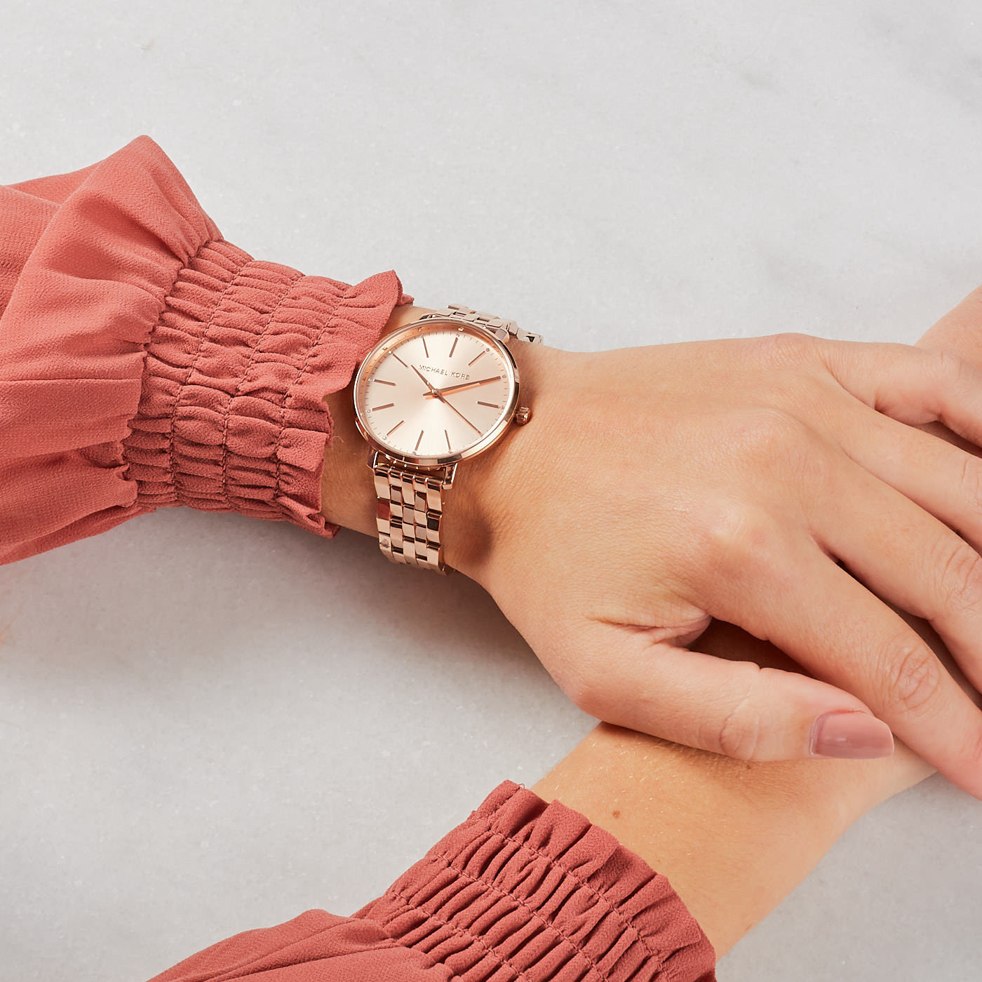 Michael Kors Pyper rose gold watch on wrist with coral sleeve, side view